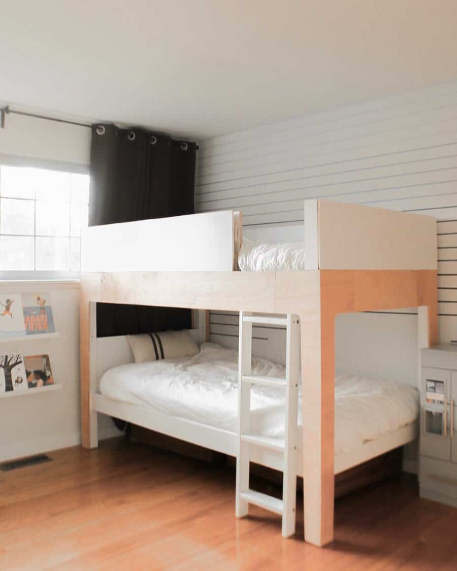 Minimalist bunk bed in light wood and white, featuring a built-in ladder and cozy lower bed setup in a bright, modern room