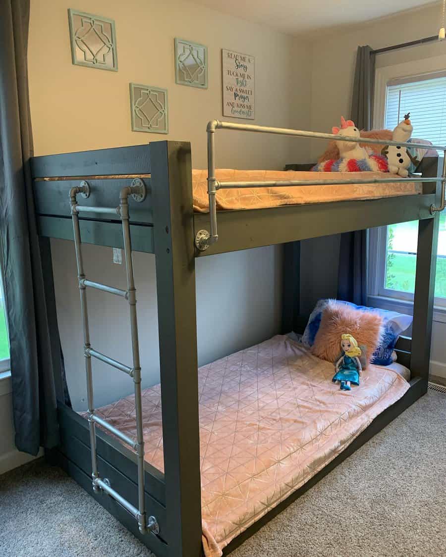 Bunk bed with dolls on top, quilt pillows on bottom; room has gray curtains, decorative wall art, and carpeted floor