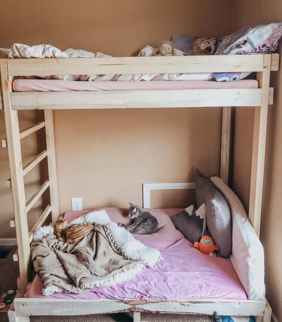 Simple wooden DIY bunk bed with a cozy lower lounge area, soft pink bedding, and furry friends enjoying a relaxed vibe