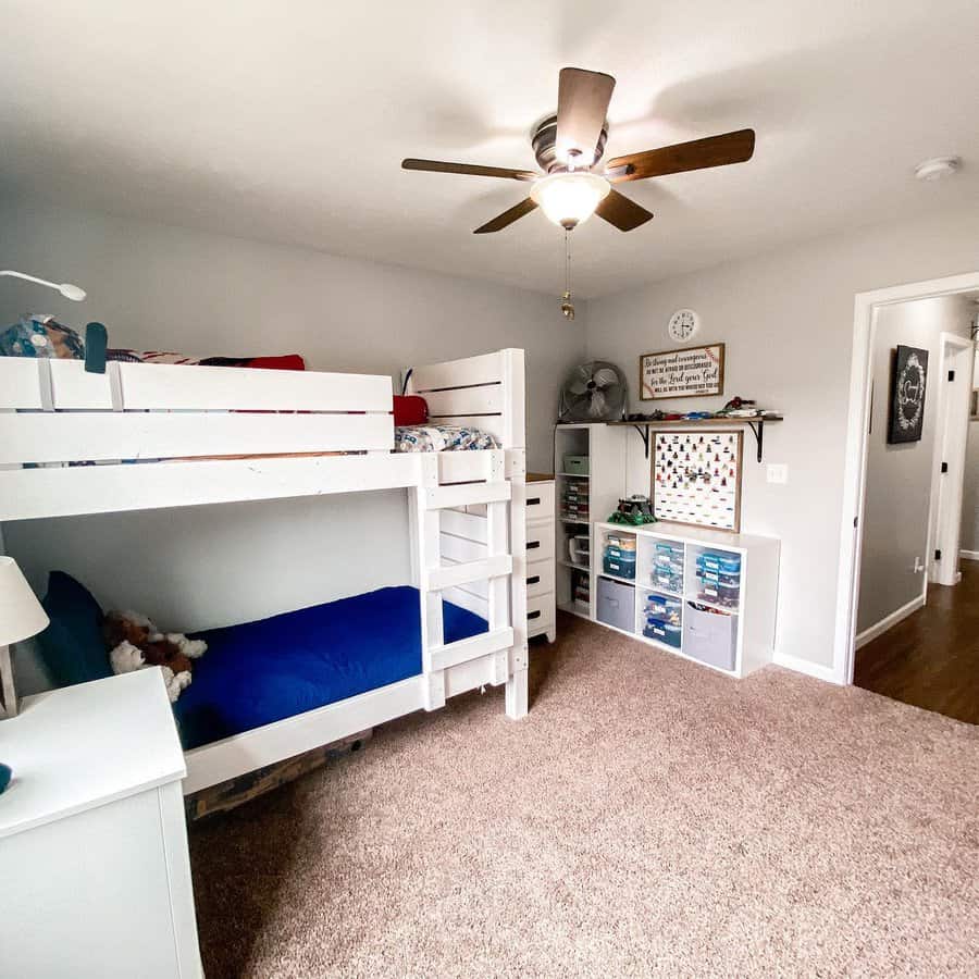 Children's room with white bunk beds, ceiling fan, brown carpet, toy storage, a dresser, and wall decor