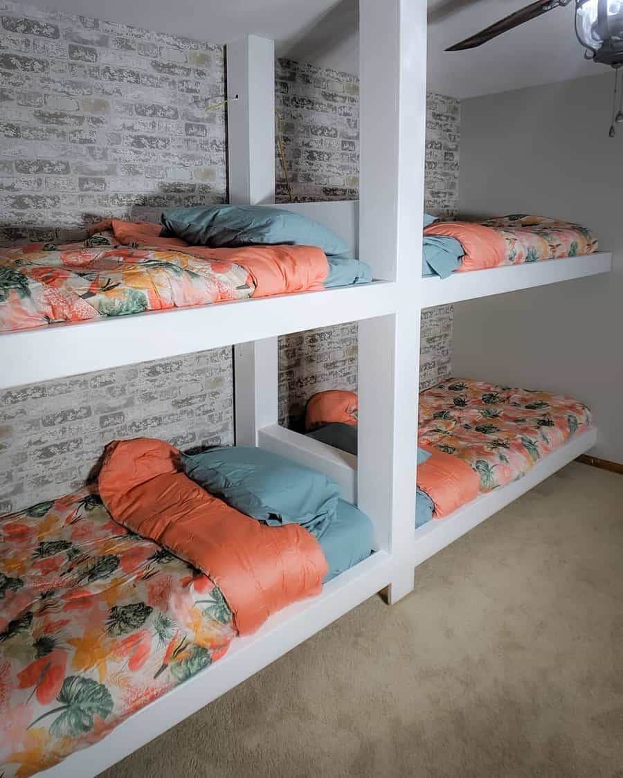 Four bunk beds with floral-patterned bedding against a brick accent wall in a carpeted room