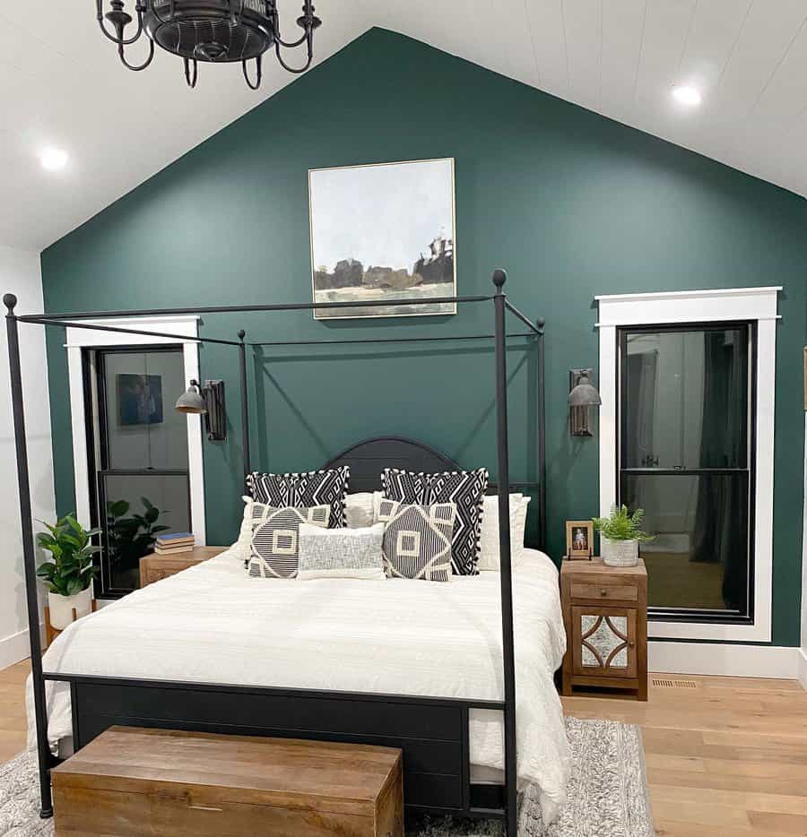 Modern farmhouse canopy bed with a sleek black metal frame, white bedding, geometric pillows, and a deep green accent wall for a cozy feel