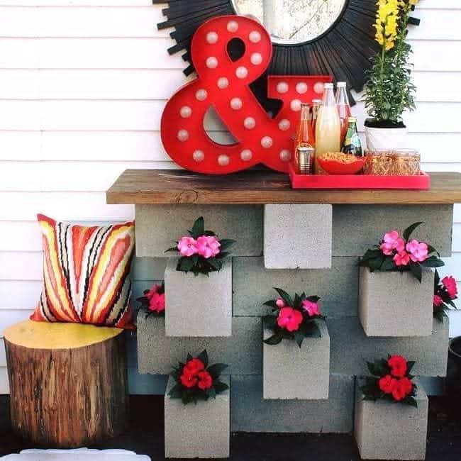 Stylish DIY cinder block bar with built-in flower planters, a wooden top, and vibrant decor, creating a functional and eye-catching outdoor setup