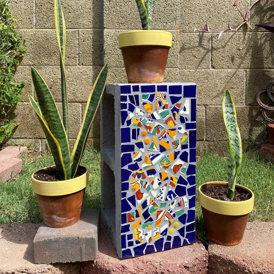 DIY mosaic cinder block planter with vibrant blue and multicolored tile accents, paired with potted snake plants for a decorative outdoor touch