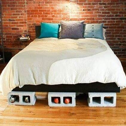 Industrial-style DIY bed frame made from cinder blocks, offering built-in storage, set against an exposed brick wall for a modern, rustic bedroom look