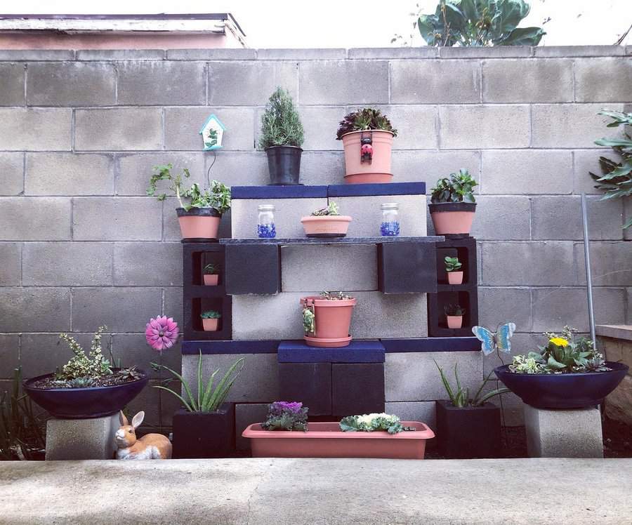 Tiered DIY cinder block plant stand with black-painted blocks and terracotta pots, creating a stylish vertical garden against a concrete wall