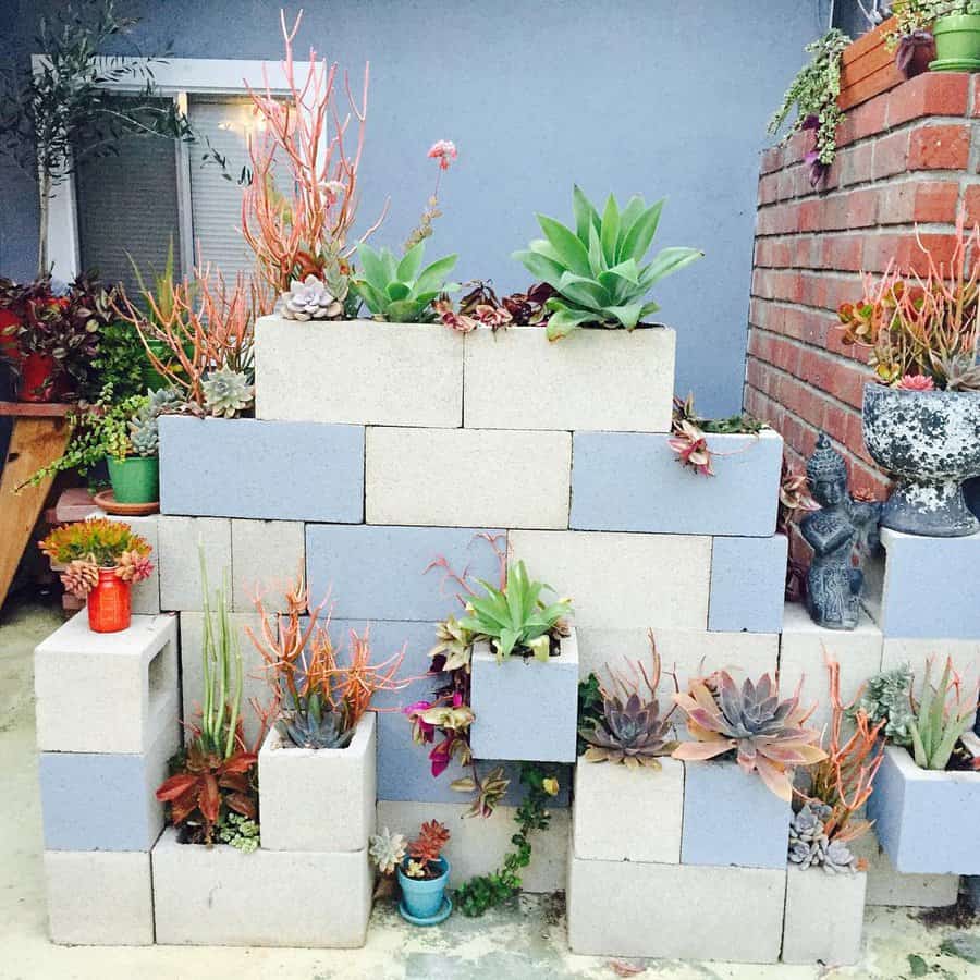 Tiered DIY cinder block planter wall with succulents and vibrant greenery, creating a stunning vertical garden against a blue house backdrop