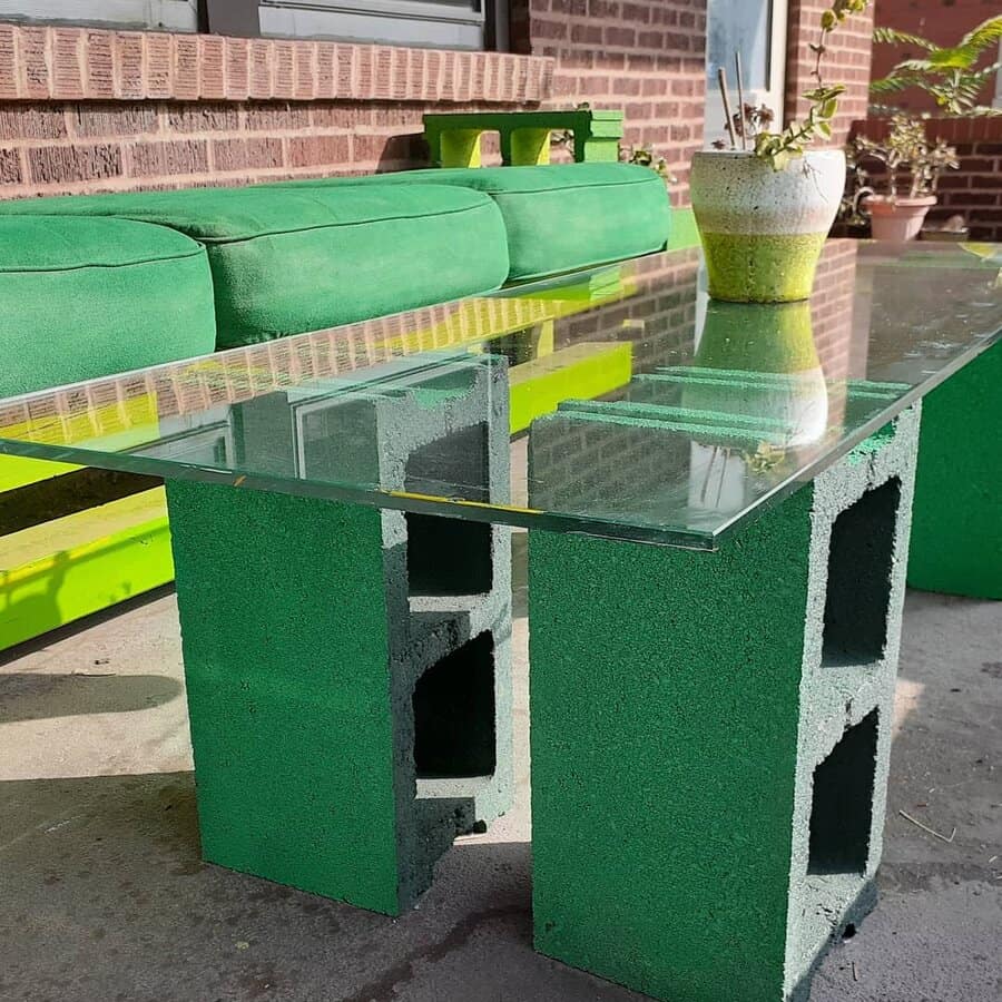 DIY outdoor table with green-painted cinder blocks as legs and a sleek glass top, paired with a matching bench for a modern and vibrant patio setup