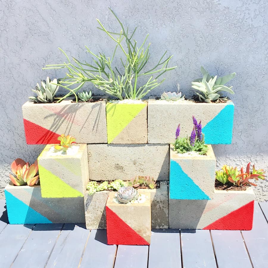 Colorful DIY cinder block planter wall with geometric red, yellow, and blue accents, showcasing succulents and greenery against a modern outdoor backdrop