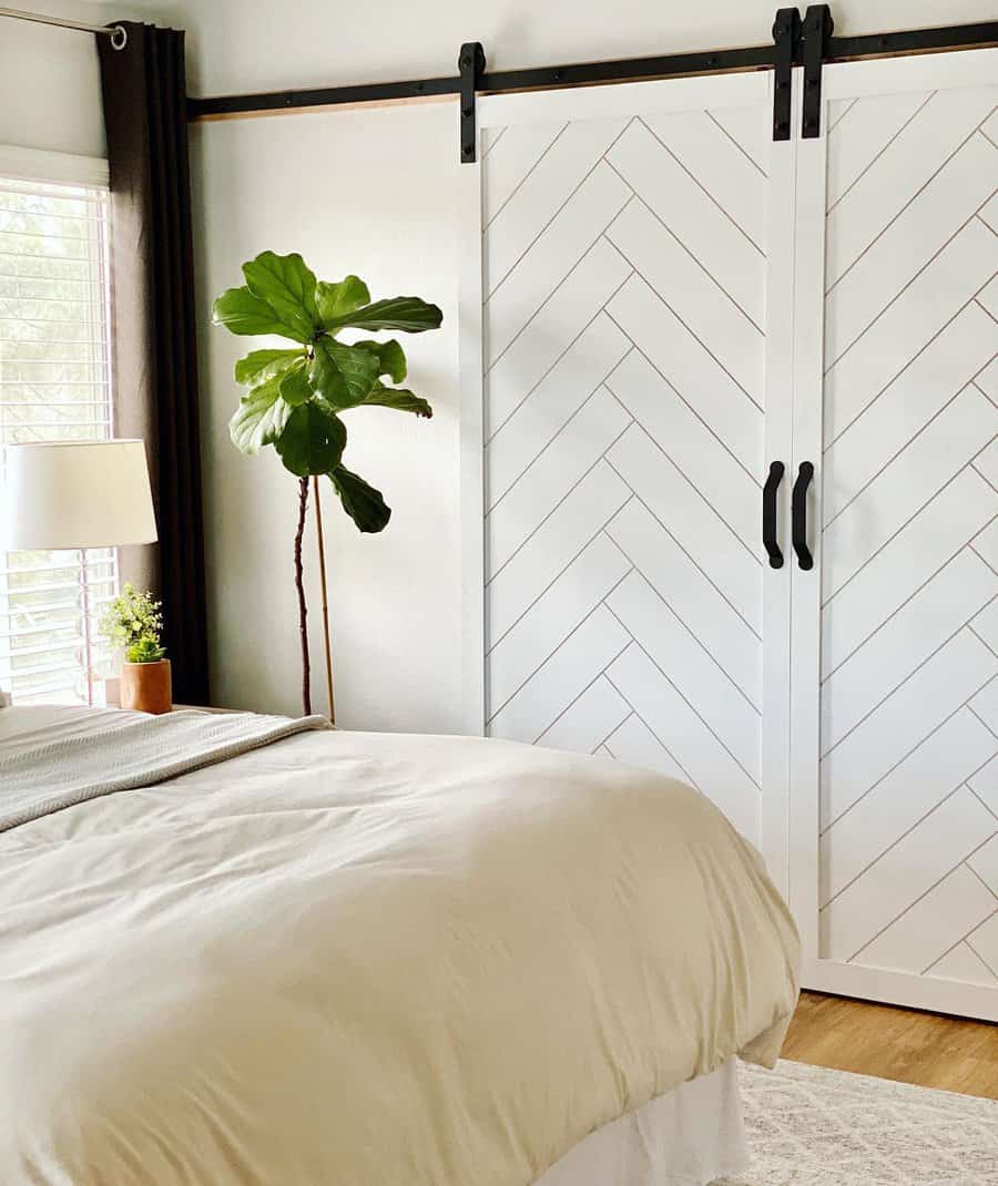 White chevron-patterned barn doors with black hardware add a stylish rustic touch to a cozy bedroom with warm neutrals and natural light