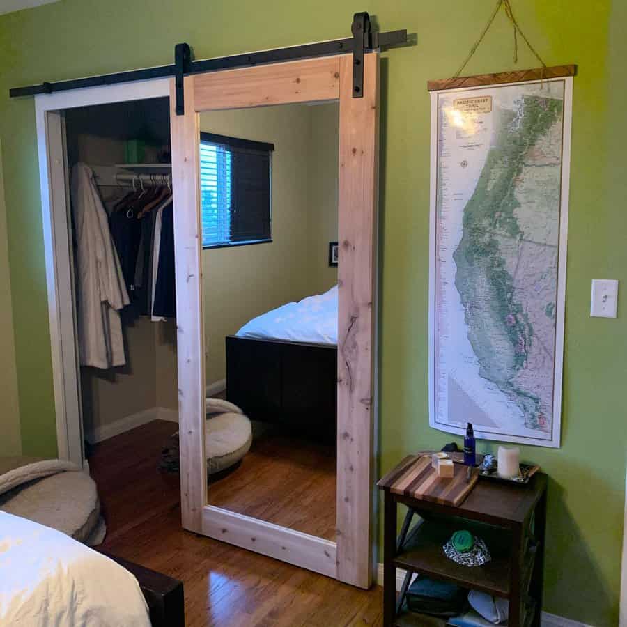 A rustic barn-style sliding closet door with a full-length mirror adds functionality and charm to a cozy bedroom with green walls and wood flooring