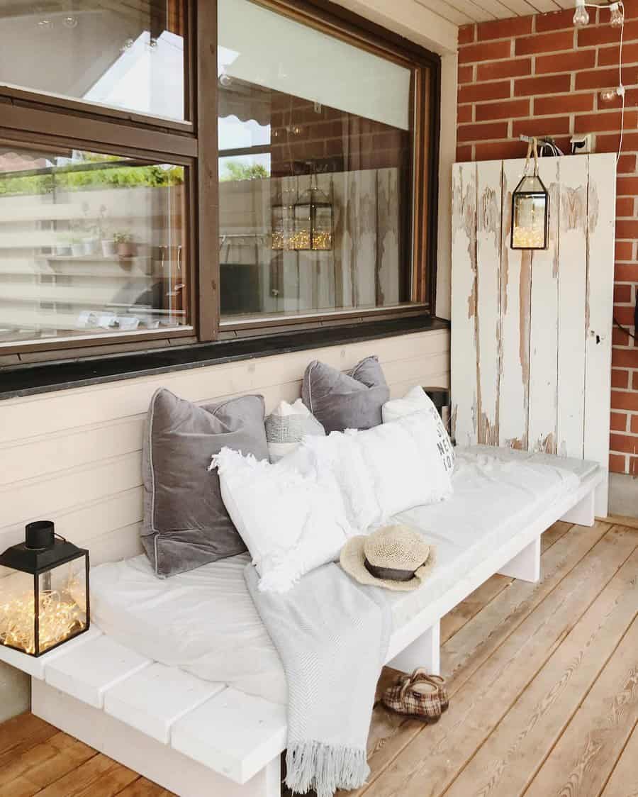 Charming DIY outdoor daybed with white wood seating, cozy cushions, a soft throw, and lantern lighting, creating a relaxing patio retreat