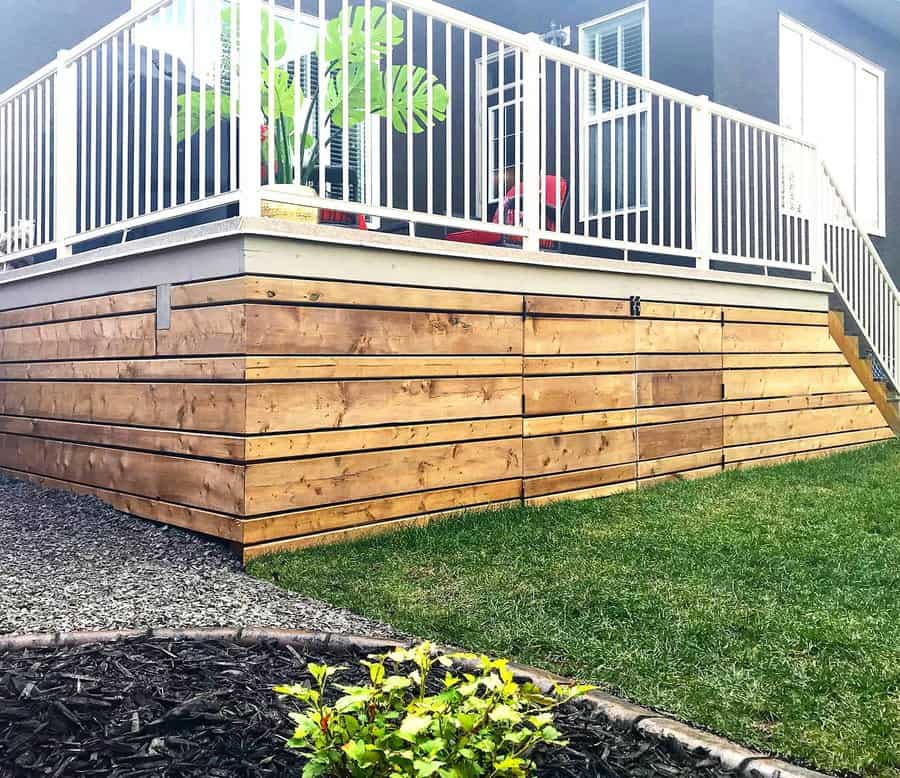 Deck with wooden skirting and white railing on green lawn