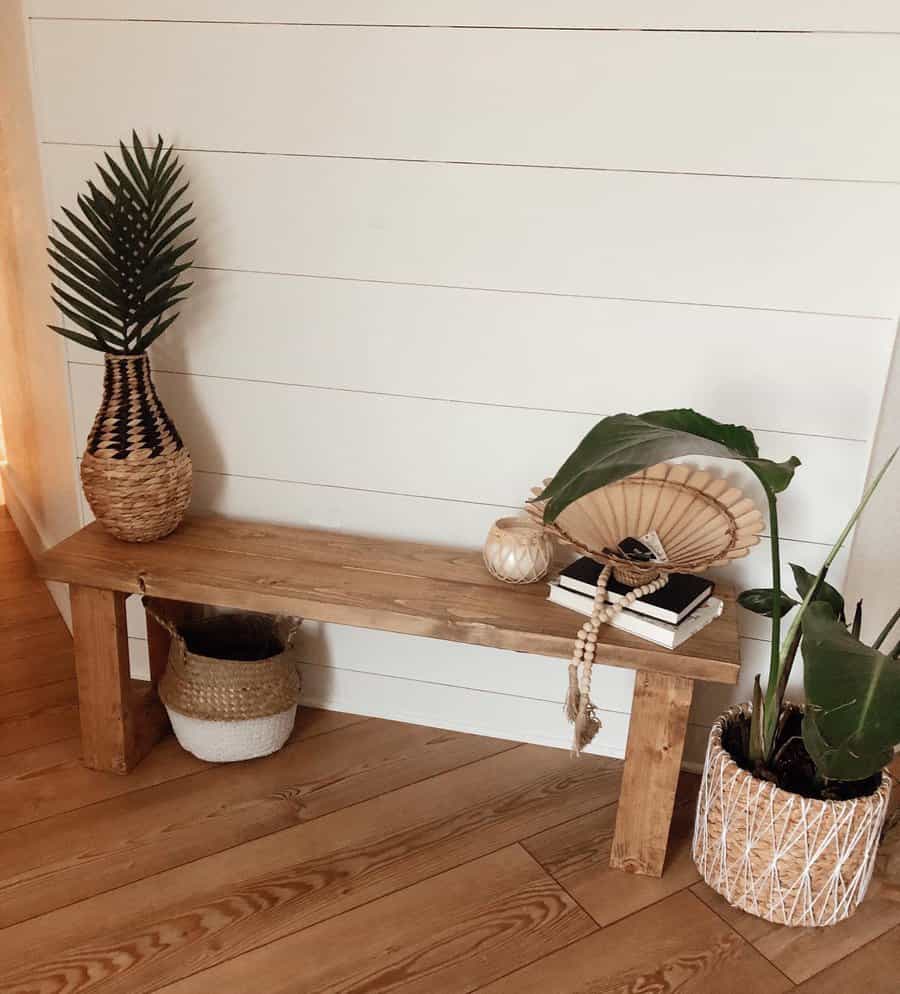 Wooden bench with a potted plant on it, surrounded by woven baskets and a plant on a wooden floor, against a white shiplap wall