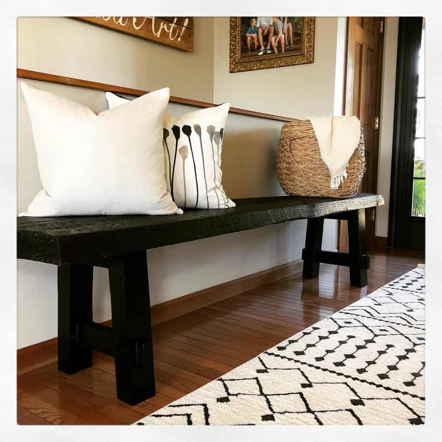 A rustic wooden bench with white and pattern pillows, beside a woven basket, and a geometric rug covering the wooden floor