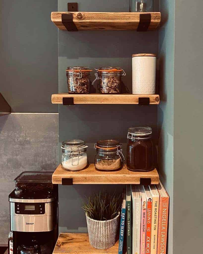 Wooden shelves with jars of ingredients, a coffee maker, plant, and cookbooks on a kitchen counter