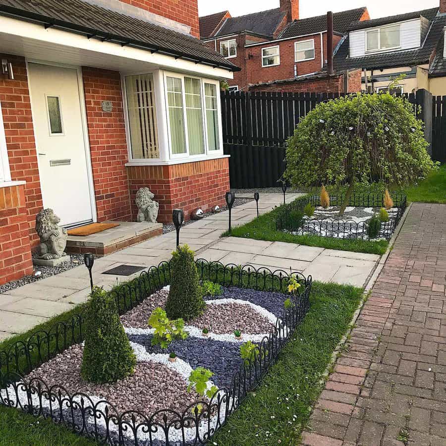 Charming front yard with decorative gravel designs, small topiary shrubs, a weeping tree, black garden edging, and brick-paved paths