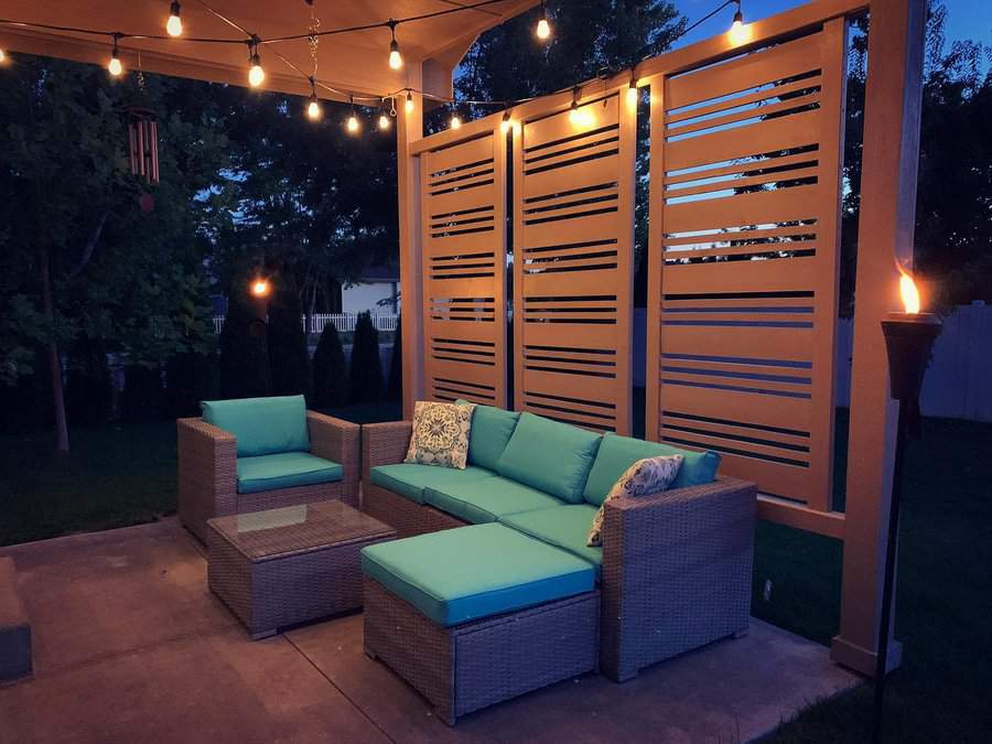 Outdoor patio with wicker furniture, teal cushions, and decorative pillows. String lights hang above, adding a warm glow to the setting