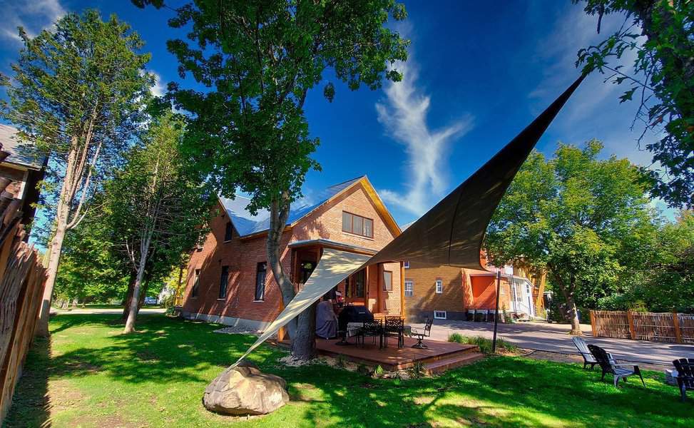 Brick house with a triangular sunshade over a patio, surrounded by trees and grass on a sunny day