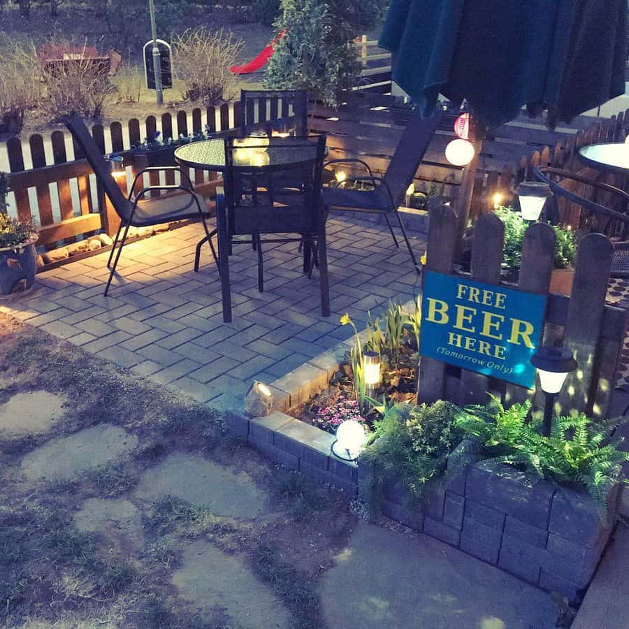 Cozy outdoor patio with tables and chairs, string lights, and a humorous "Free Beer Tomorrow" sign on the fence