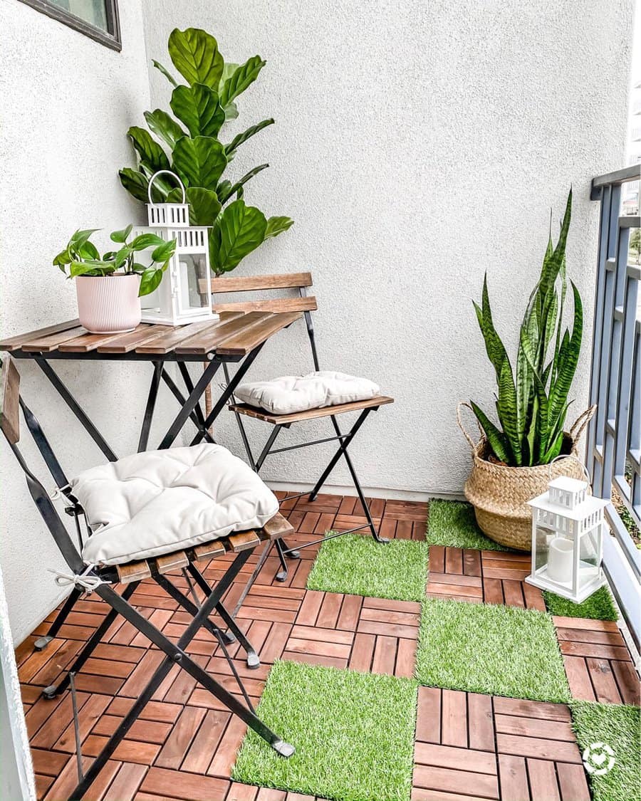 Cozy balcony with two chairs, a small table, potted plants, and lanterns on wooden tile flooring with green grass patches