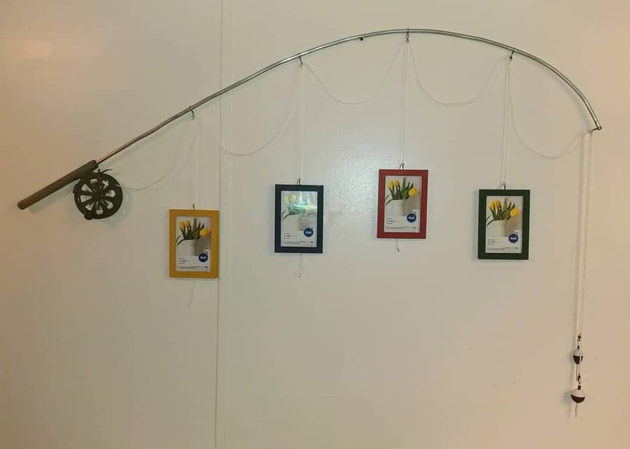 Fishing rod on a wall with picture frames hanging from it, each frame a different color, resembling a catch of photo memories