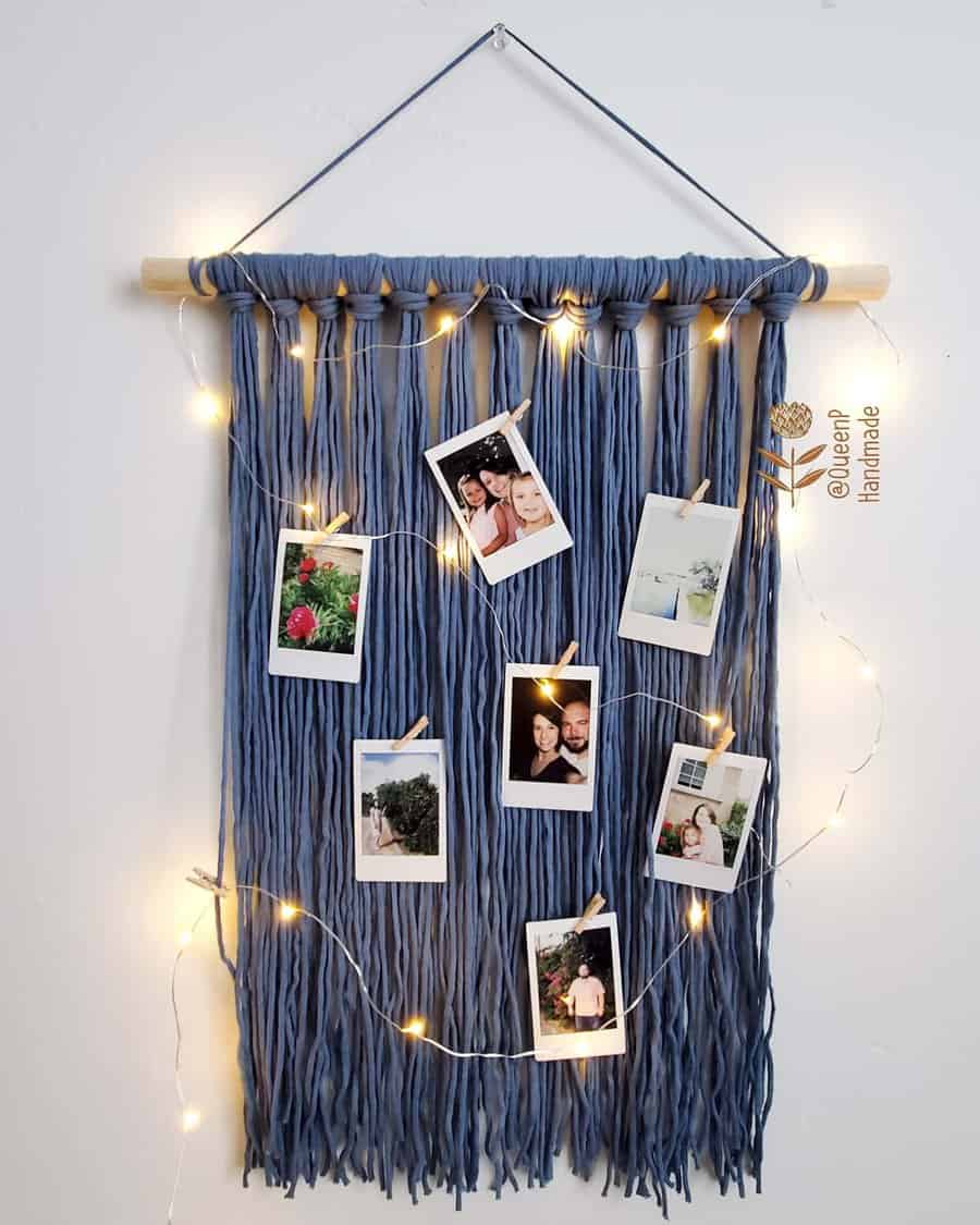 A blue macramé photo display with hanging lights and polaroids attached, adorned on a white wall