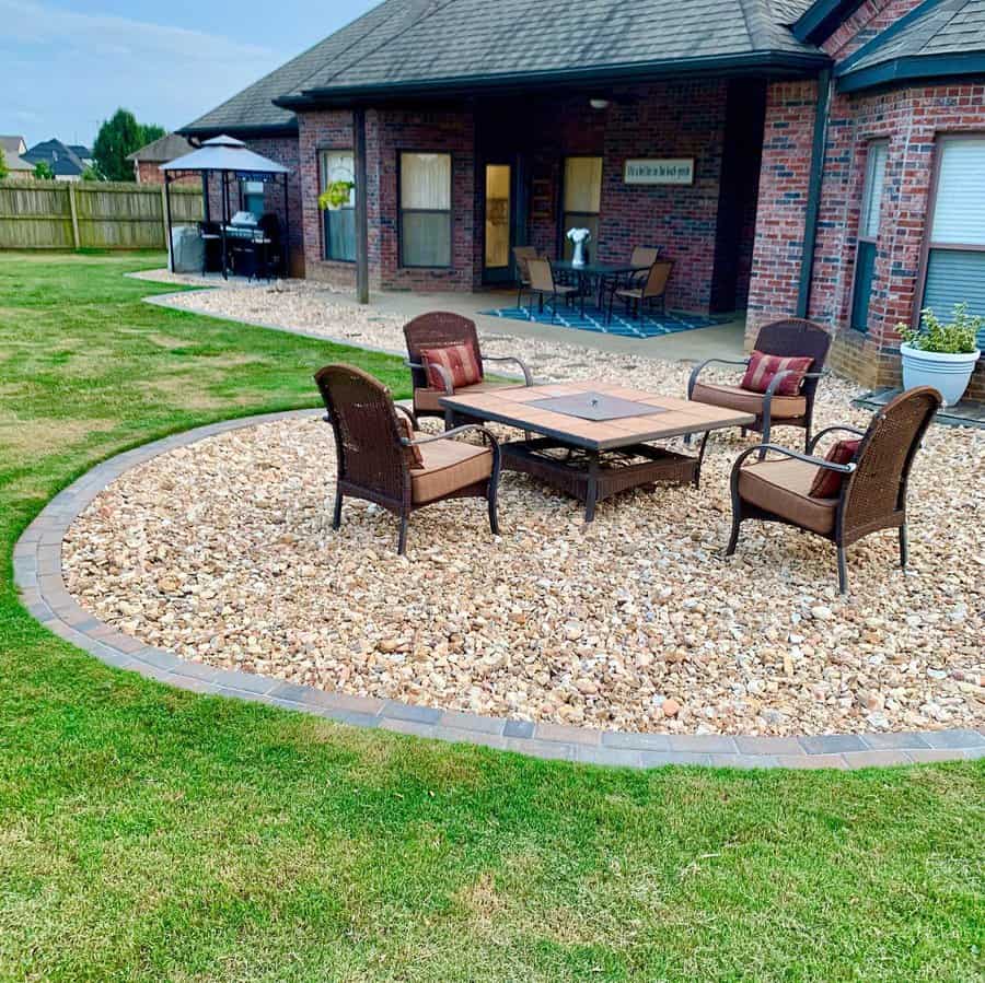 Backyard seating area with a circular gravel patio, wicker chairs, a fire pit table, and a brick house with a covered dining space