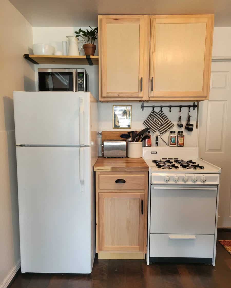 Compact kitchen with wooden cabinets, a small stove, a white fridge, and smart storage solutions like hanging utensils and open shelves