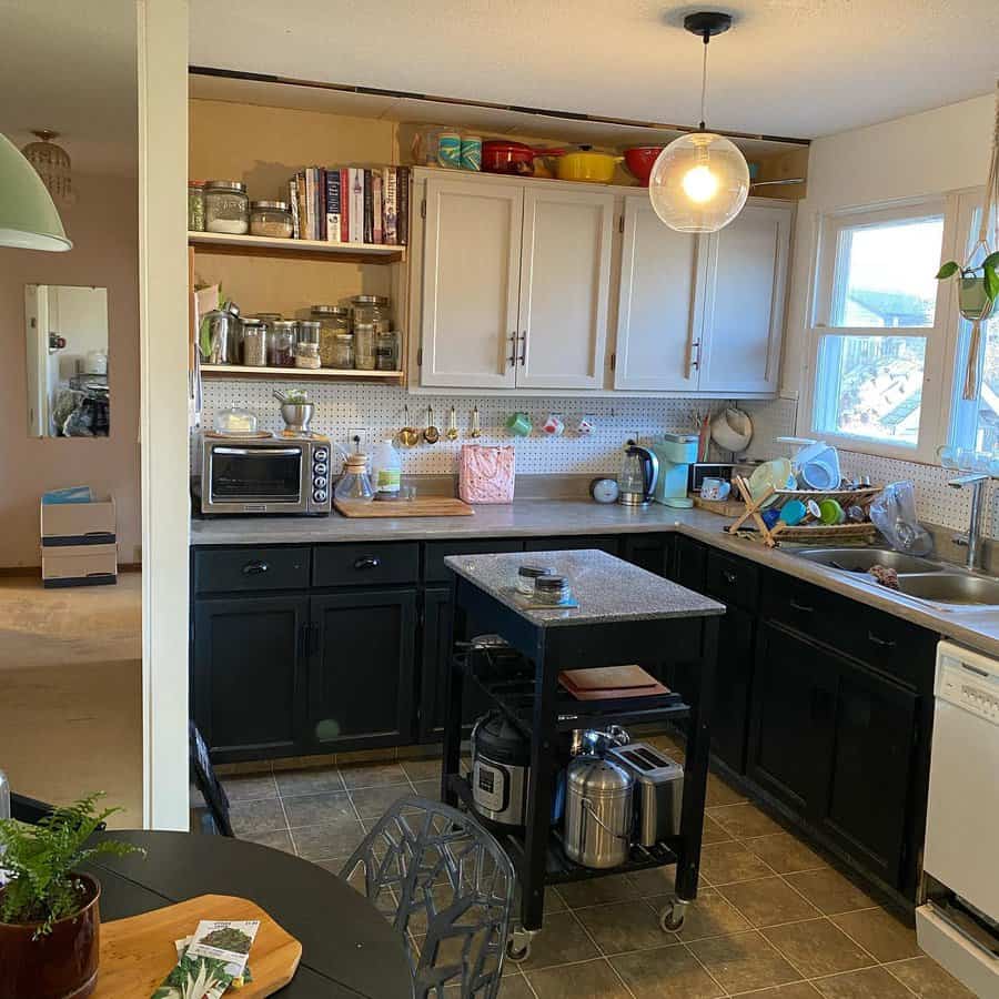 Cozy kitchen with black and white cabinets, open shelving for jars and books, a rolling island, and pegboard storage for utensils