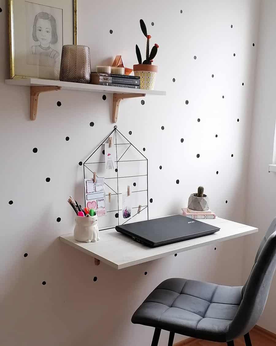 Minimalist workspace with a floating desk, laptop, chair, and shelves; decor includes cacti, a wall organizer, and a dotted wall pattern