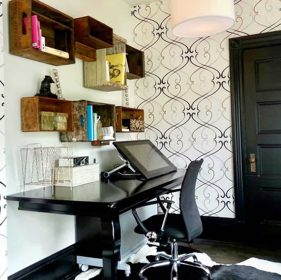 Home office with a black desk and chair, wall-mounted wooden shelves, decorative wallpaper, and a digital drawing tablet on the desk