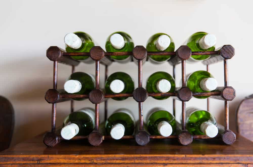 Wooden wine rack holding twelve green wine bottles with white caps, arranged in three rows on a wooden surface