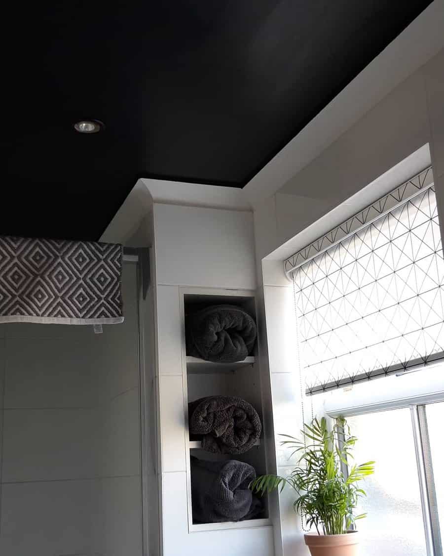 Modern bathroom with a bold black ceiling, white walls, and geometric accents, creating a sleek contrast with built-in towel storage and natural light.