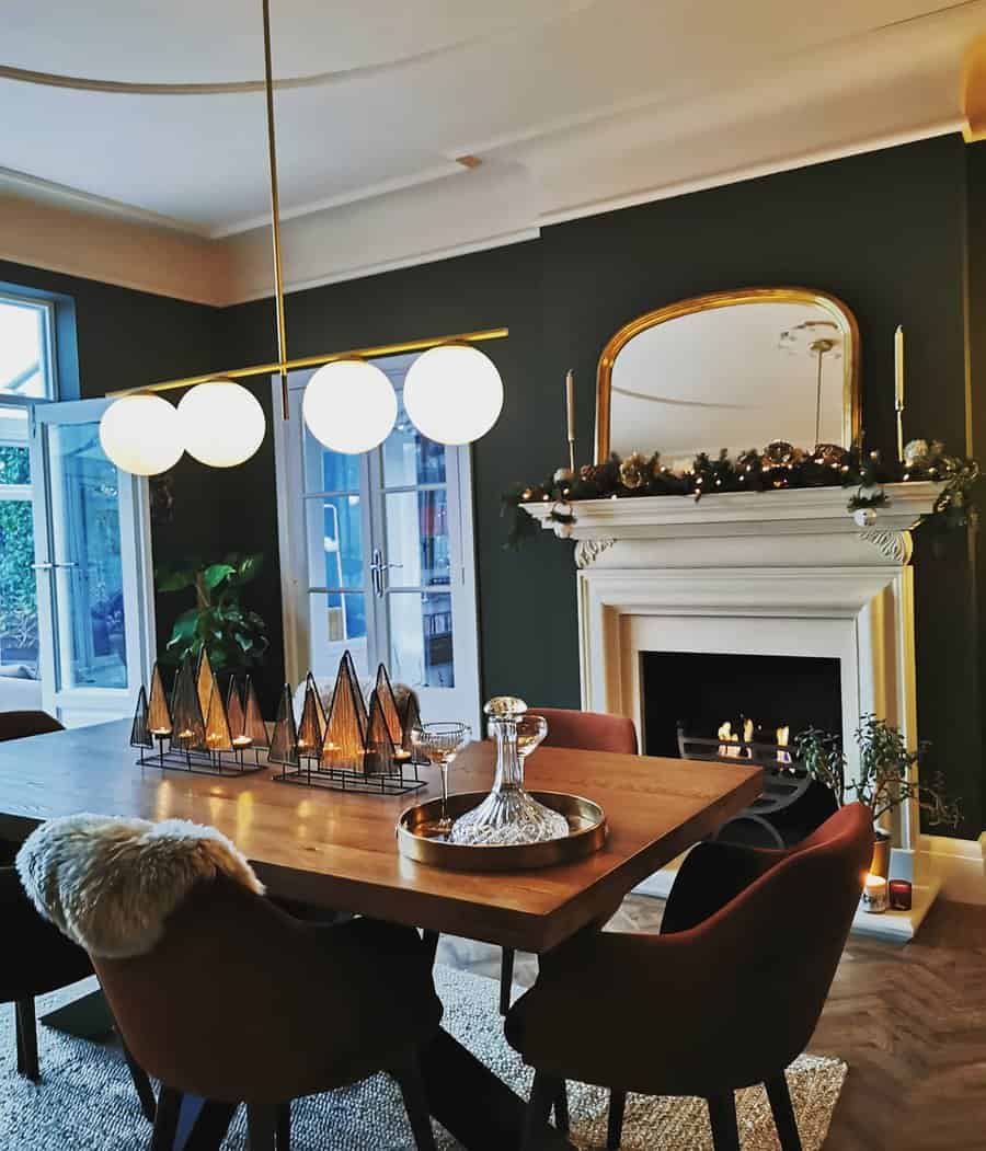 Cozy dining room with dark walls, a wooden table, modern chairs, and a lit fireplace adorned with a garland and candles