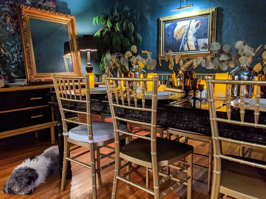 Elegant dining room with gold chairs, a dark table set, abstract art, and a furry dog resting on the wooden floor