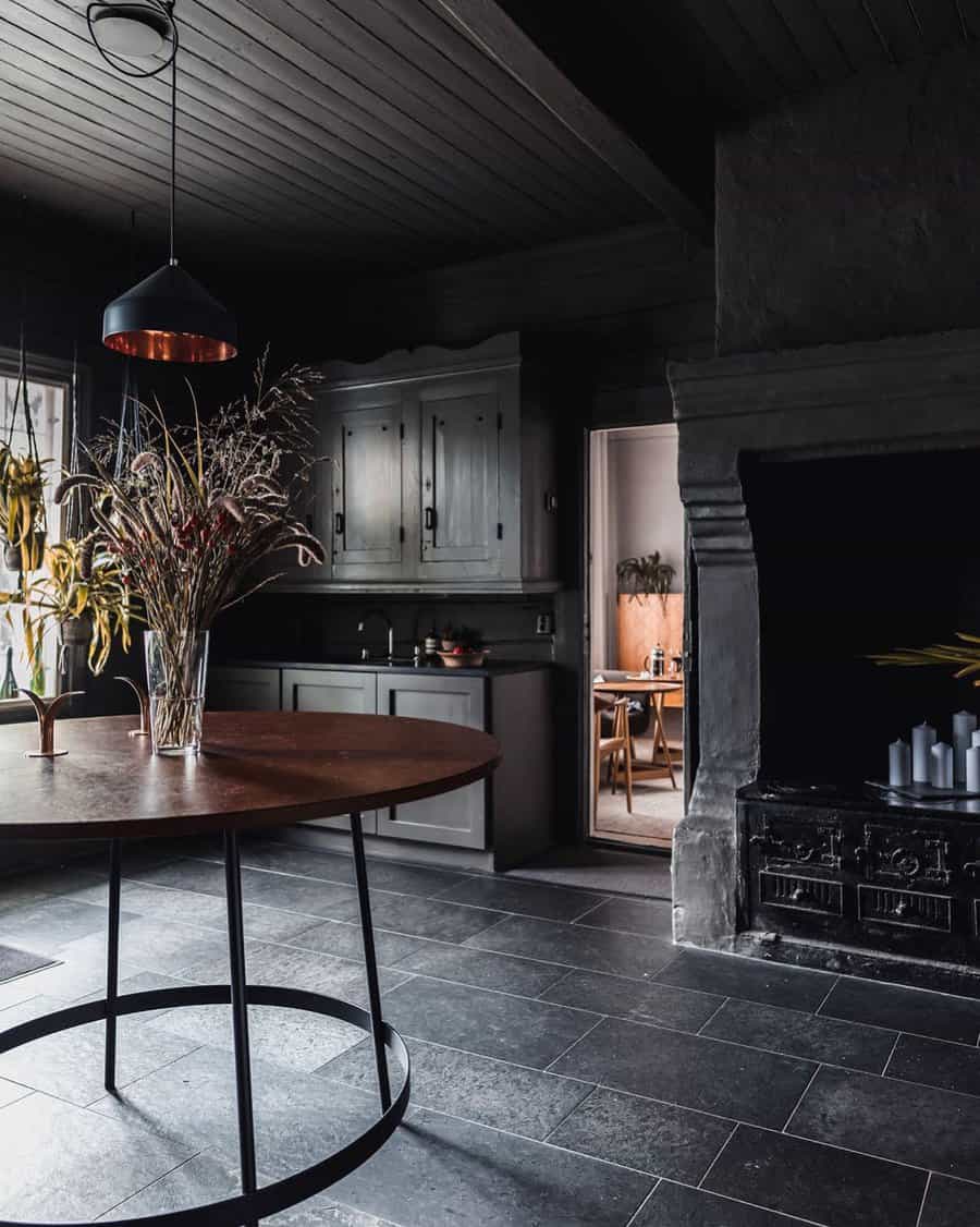 Dark stone tile flooring enhances this moody, rustic kitchen, complementing black cabinetry and warm wood accents for a sophisticated look