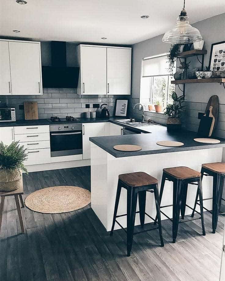 Dark wood-style flooring grounds this modern kitchen, complementing white cabinetry and black countertops for a sleek, balanced contrast