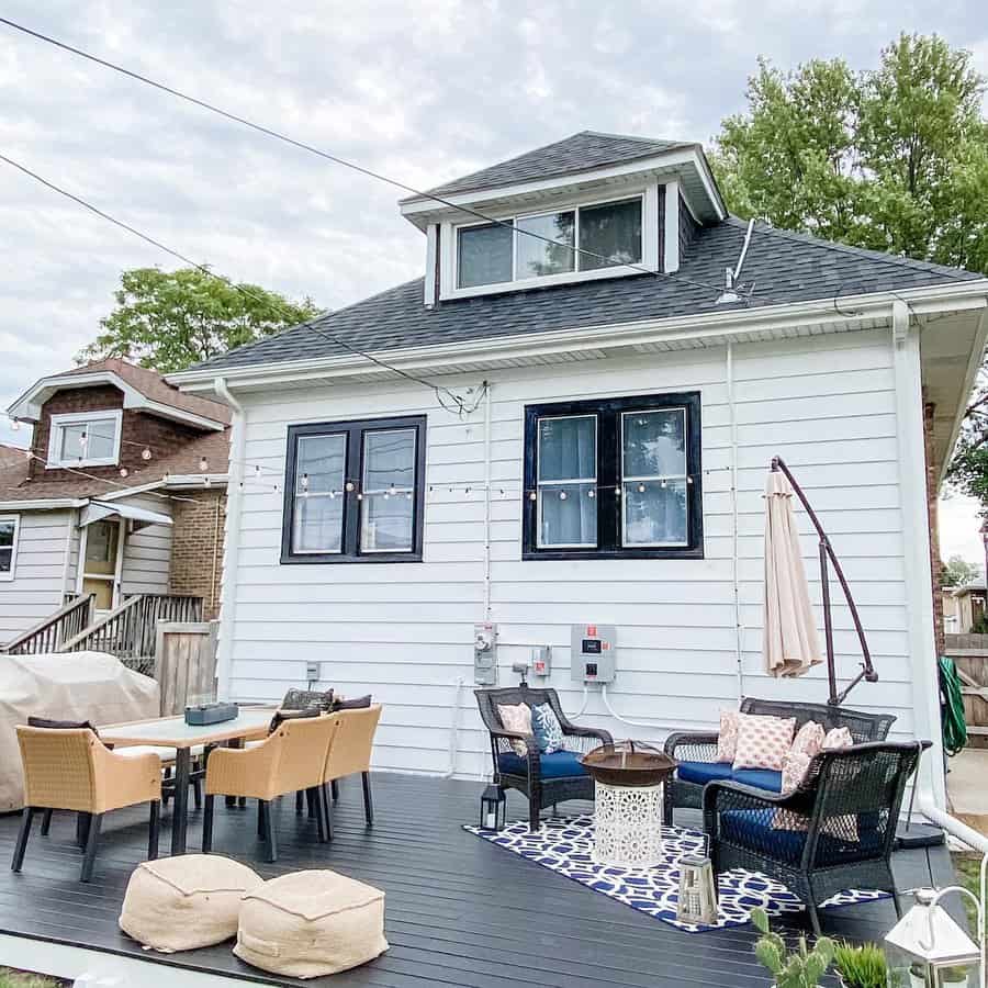 Cozy backyard with patio furniture, string lights, and a black raised deck; white house in the background with dark trim windows