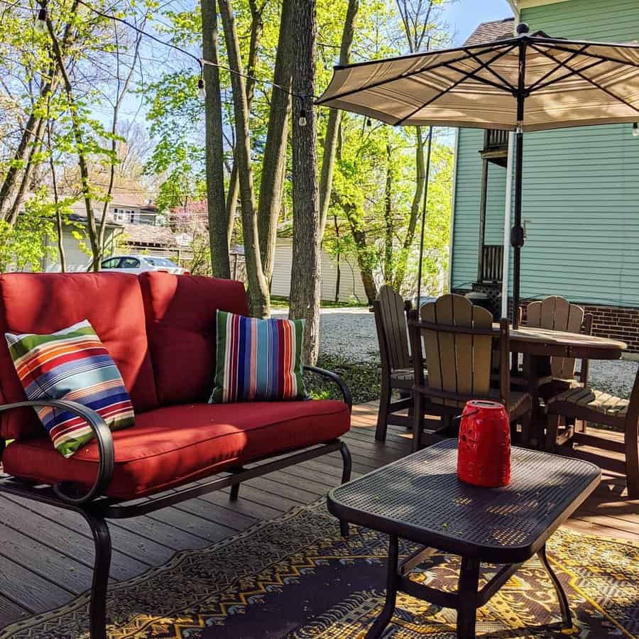 Outdoor deck with red cushioned seating, striped pillows, a table with a red lantern, and a dining set under a large umbrella