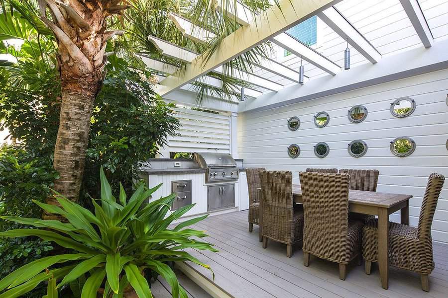 Tropical outdoor dining area with a pergola-covered deck, rattan chairs, built-in grill, and lush greenery for a shaded retreat