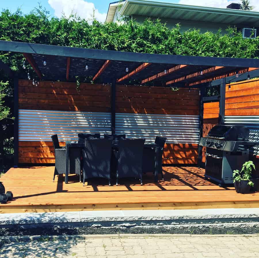 Modern pergola-covered deck with a dining area, built-in grill, wood and metal privacy panels, and string lights for a stylish outdoor space