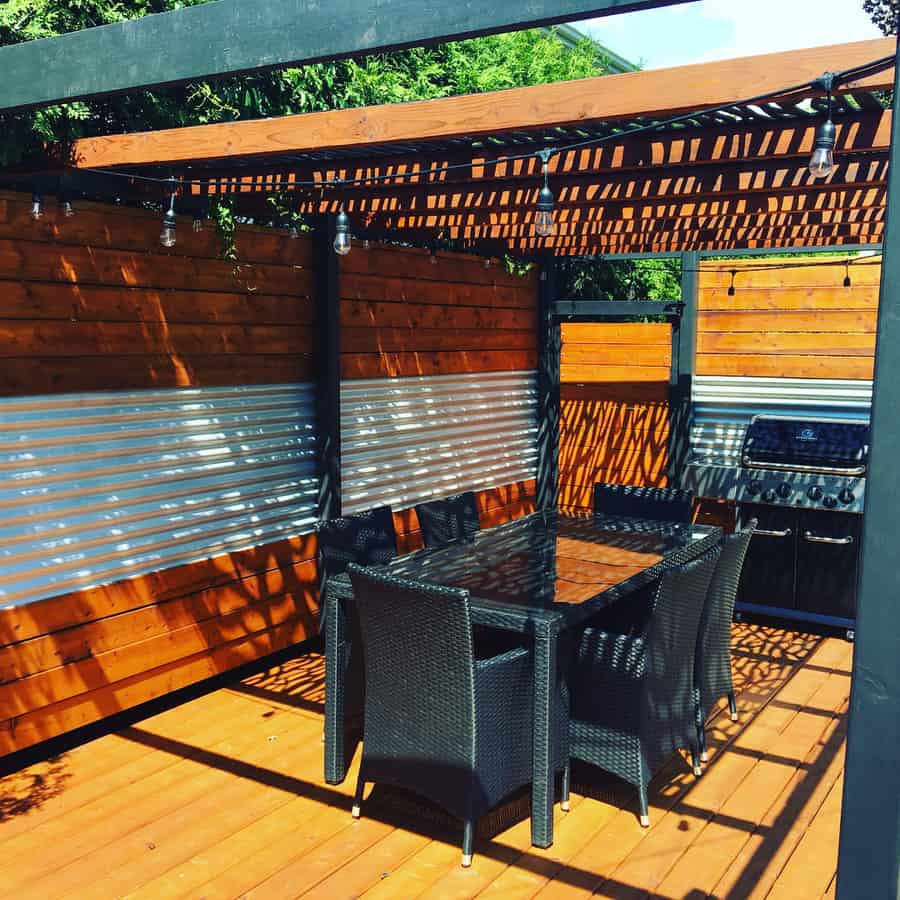 Outdoor patio with a wooden pergola, string lights, and a dining set on a wooden deck, complemented by corrugated metal panels that add a modern touch