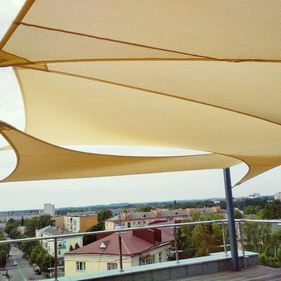 Rooftop terrace with multiple beige shade sails, offering sun protection and a scenic view of the city below