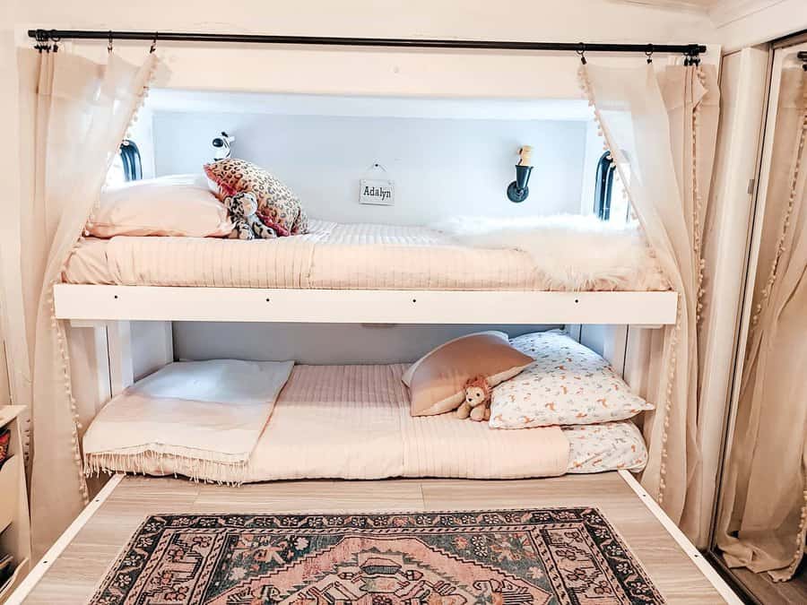 Cozy bunk beds with pastel bedding and curtains, decorative pillows, stuffed animal, wall light, and patterned rug below