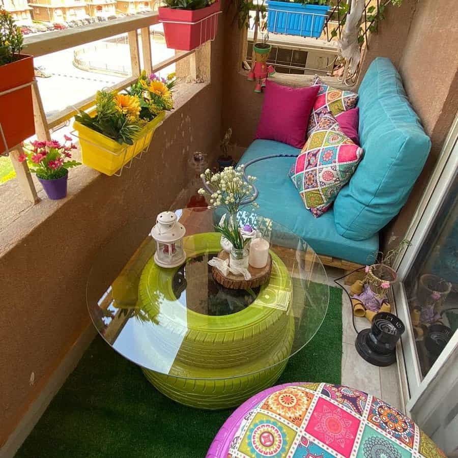 Vibrant small balcony with colorful cushions, a DIY tire table with glass top, hanging planters, and a cozy seating area