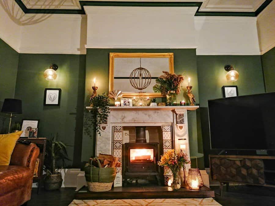 A stylish fireplace with a marble mantel, warm lighting, green walls, and decorative plants, creating a cozy and inviting ambiance