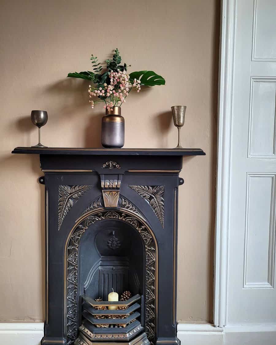 A vintage black fireplace with a floral design, adorned with a vase of flowers, candles, and gold accents for a charming, elegant look