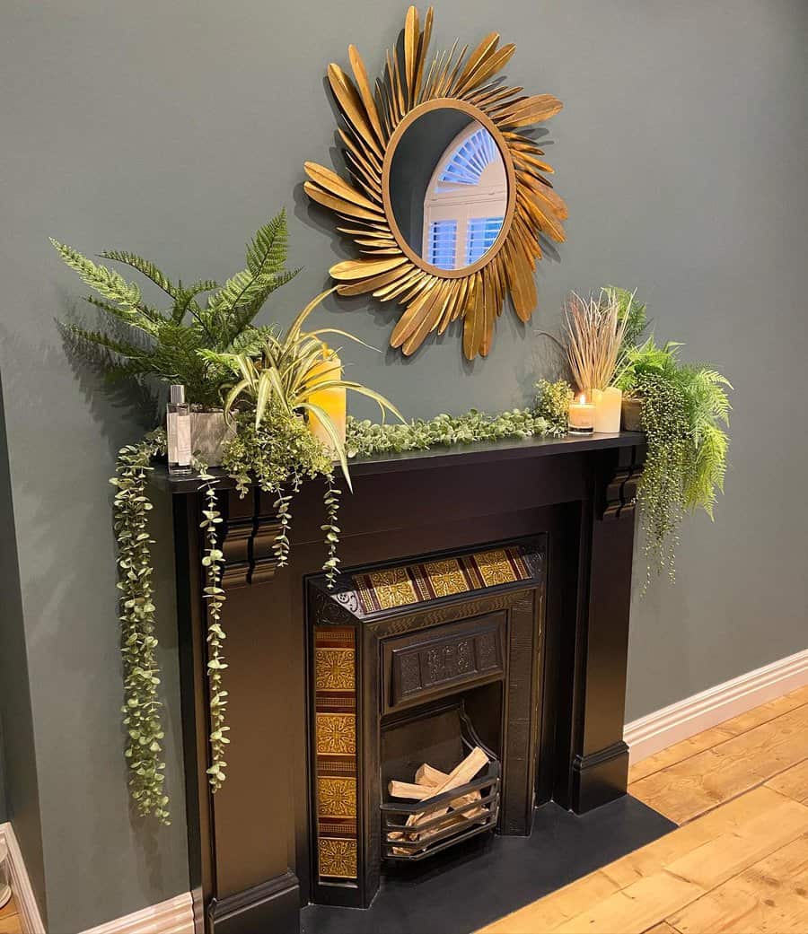 A sleek black fireplace with a gold-accented tile, surrounded by lush greenery, a large decorative mirror, and candles for a fresh, modern look