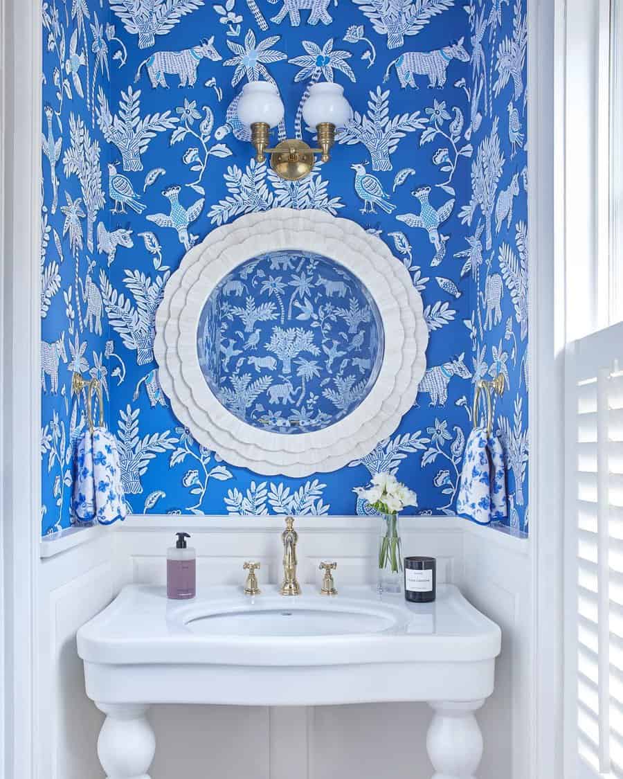 Elegant blue and white bathroom with intricate floral wallpaper, round mirror, vintage-style sink, and brass fixtures